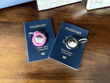 Two AirTags in pink and black placed on our passports for luggage tracking and travel peace of mind