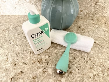 Cerave cleanser and PMD brush on a bathroom counter with white towel, representing gentle daily clea