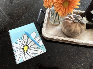 Personalized notebook on a kitchen island with orange flowers and a small pumpkin as fall decor