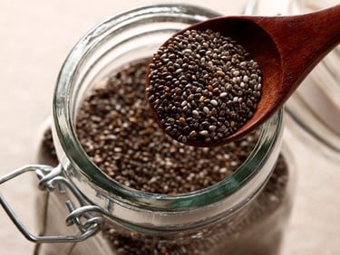 Jar of chia seeds with a wooden spoon scooping out a serving size to show portion and texture.