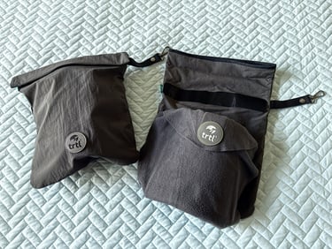 Two trtl pillows, one inside the travel bag and one gray pillow on top with the black strap visible 