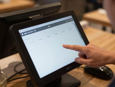 Close-up overhead shot of a restaurant POS touchscreen mid-order entry, hands visible on screen, table number displayed, ambient kitchen warmth in background