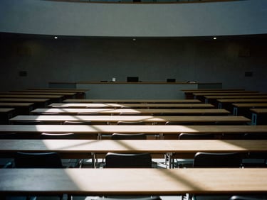 Wide-angle architectural shot of an empty international assembly hall, hard directional light casting long dramatic shadows across rows of empty desks, desaturated cool tones, 35mm film grain.