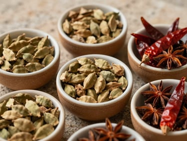 Ceramic bowls filled with whole spices—cardamom pods, dried red chilies, star anise—arranged on a rough stone surface, soft natural daylight, warm ochre tones, close-up overhead framing