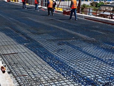 Close-up of fresh concrete being poured onto steel reinforcement mesh on a highway bridge deck, construction workers in high-vis vests and hard hats supervising, high-contrast daylight.