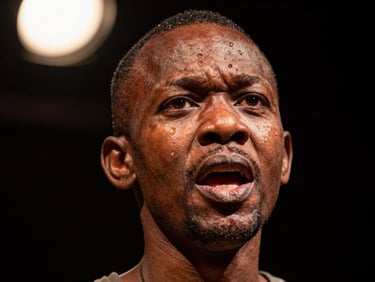 Intimate close-up of a theatre actor's face in a moment of intense dramatic expression under a single warm spotlight, deep dark background, Kinshasa theatre company production