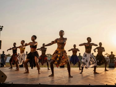 Wide environmental shot of a contemporary African dance ensemble mid-performance on an open-air stage at golden hour, bodies caught in full extension, warm amber light flooding the space, Lomé arts festival