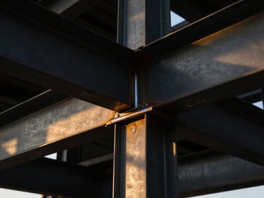Detailed close-up of a steel beam junction in an industrial setting, with sharp focus on the welds and structural integrity, dramatic directional lighting casting long shadows.