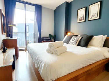 Modern hotel bedroom with a king-size bed, white linens, and blue accent wall near a private balcony.