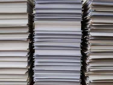 Close-up of stacked, neatly organized physical archival documents, labeled with institutional names, soft library light, muted corporate tones, editorial documentary photography.