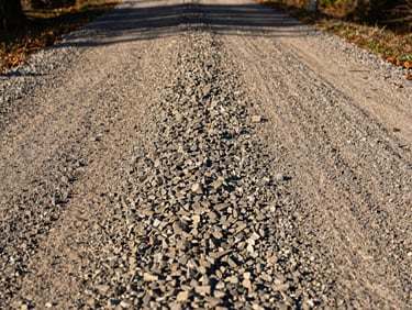 Low-angle shot of a freshly graded gravel driveway in Northeast Georgia, sharp focus on compacted stone texture under bright morning sunlight