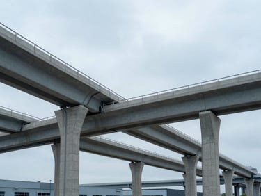 Wide environmental shot of modern infrastructure, concrete bridge pillars and clean industrial structures under overcast slate skies