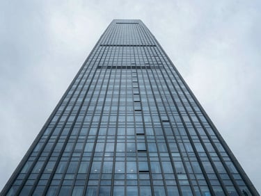 Wide-angle architectural perspective of a towering modern commercial skyscraper, sharp glass facade reflecting overcast sky.