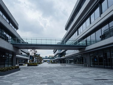 Modern architectural structure featuring glass walkways and outdoor plazas, overcast daylight, desaturated blue tones