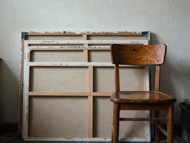 A quiet, front-facing elevation of an artist's studio corner in Manila, with stacked canvases and a single wooden chair.