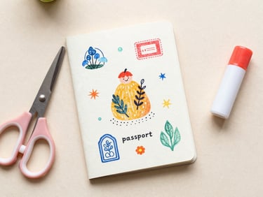 Overhead flat-lay of a hand-crafted paper passport with colorful stamps, sitting next to safety scissors and a glue stick on soft textured paper, warm diffused natural light.
