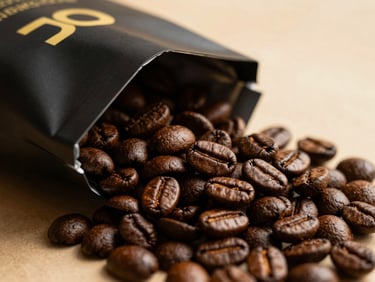 Macro shot of glossy dark roasted Arabica coffee beans spilling out of a minimalist matte-black bag with gold foil lettering, warm side-lighting
