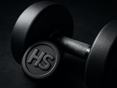 Dramatic close-up of a matte-finished premium dumbbell showing precise HS branding, strong directional key light, deep charcoal and metallic tones, sharp focus, 50mm.