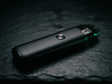Cinematic macro shot of a sleek matte black vape device on a dark slate counter, subtle emerald green backlighting, rich shadows