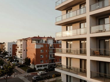 Warm editorial architectural photography, soft natural morning light, muted earthy tones, realistic 35mm lens. A contemporary condominium balcony overlooking a vibrant neighborhood, showing architectural details.