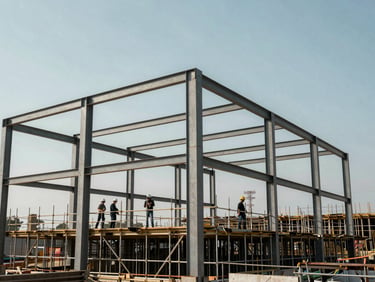 Wide shot of a construction site at daylight showing steel structural framework rising against a clear sky, workers in hardhats visible mid-frame on scaffolding