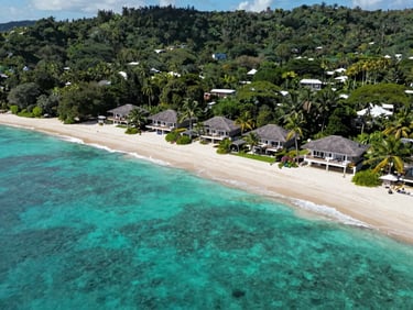 Aerial view of luxury villas on a secluded private peninsula in Nosy Be, turquoise ocean waters, lush tropical forest surrounding the white sand beach.