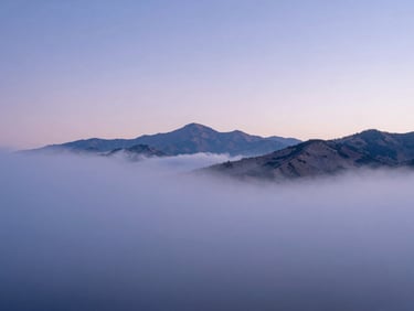 Soft-focus view of misty Utah mountains at dawn, light blue and lavender hues filtering through low-hanging clouds, quiet and expansive landscape.