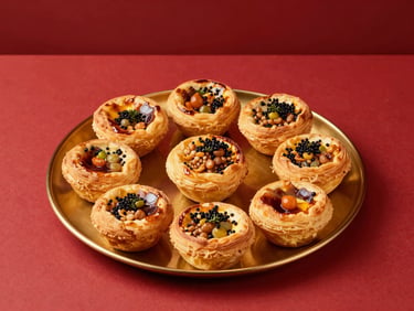 Top-down view of neatly arranged gourmet savory pastries on a polished gold platter, minimalist red backdrop, sharp studio light.