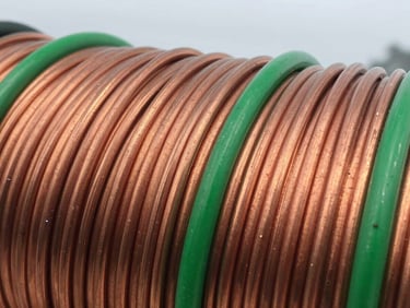 Close-up of clean, shiny copper wires neatly coiled in an industrial setting, bright overcast daylight, sharp focus, 35mm, clean metallic tones with vibrant green accents