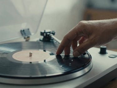Close-up of hands adjusting a vinyl record player, warm diffused lighting, dust particles floating in air, 35mm film grain.
