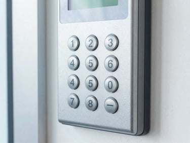 Close-up of an access control keypad with a clean metallic finish, mounted on a brushed steel frame, bright cool indoor lighting.