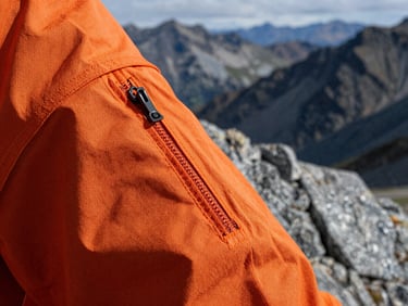 Extreme close-up of heavy-duty orange technical fabric seam under harsh alpine daylight, sharp textures, 35mm