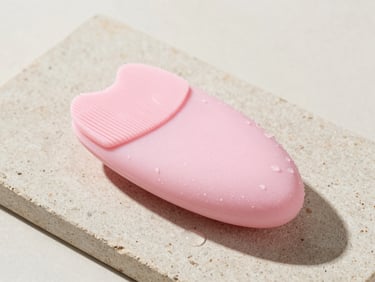 Soft pastel pink silicone facial cleansing device on a wet stone tile, water droplets, clean studio lighting, 50mm lens