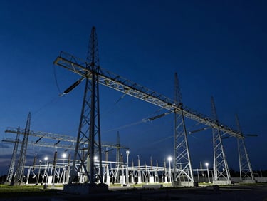 Wide-angle architectural shot of a massive high-voltage grid substation at blue hour, sharp clean steel beams against deep navy sky.