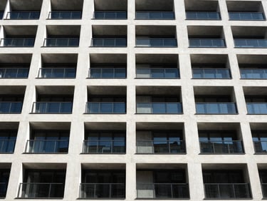 High-contrast shot of a modern multi-residential building facade, strong geometric lines, natural light, deep shadows.