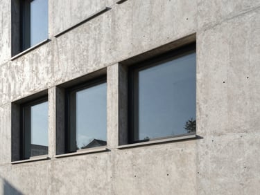 Close-up detail of a high-performance, insulated facade with raw, tactile materials like concrete and timber, under crisp morning light.