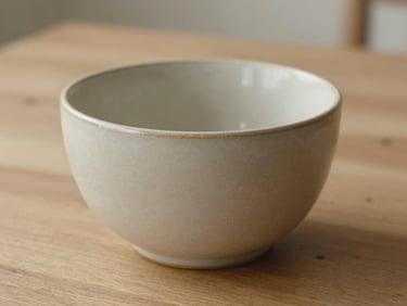 Close-up of neutral-toned ceramic stoneware on a natural wood table, soft diffused light, focusing on texture and material quality.