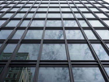 Low angle architectural shot looking straight up at a structural glass facade of a modern corporate building, dark aluminum mullions