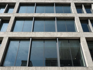Structural glass facade on a modern concrete building, looking straight up, clean reflections, sharp linear shadows.