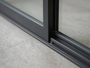 Tight macro shot of a flush-mounted minimalist floor track for sliding glass doors, black anodized aluminum finish, dust-free concrete groove