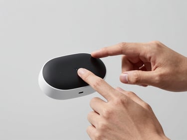 Hands interacting with a sleek, minimalist AI assistant device, natural light, light gray background, sharp details, high-contrast, 85mm lens