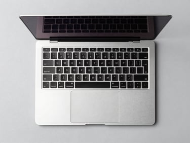 Clean top-down desk setup with a thin, modern laptop open, crisp studio lighting, light gray background, sharp details, high-contrast, 85mm lens