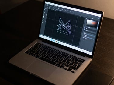 Overhead tight shot of a laptop displaying a Figma UI design canvas, cool monitor glow on a dark desk, geometric grid lines visible on screen, keyboard partially in frame