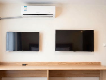 Straight-on eye-level shot of a functional hotel room interior, showing a clean desk, wall-mounted TV, and air conditioning unit.