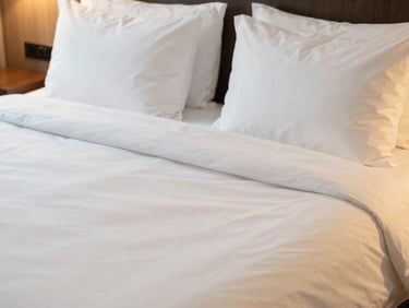 Close-up interior shot of a freshly made hotel bed with pristine white sheets and fluffy pillows, warm natural lighting, spotless.
