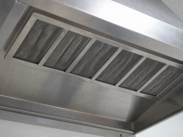 Close-up of a commercial stainless steel exhaust hood, showing clean baffle filters and brushed steel texture, cool metallic lighting