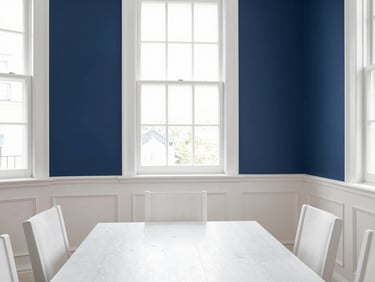 Bright editorial photography of a beautifully painted dining room with crisp white wainscoting and deep navy blue walls, sharp natural daylight streaming through a large window, highlighting flawless trim lines and immaculate paint finishes, 35mm architectural lens.