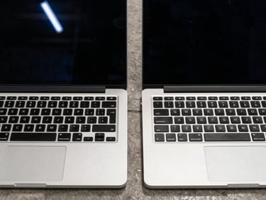 Close-up overhead shot of two open laptops side by side on a concrete floor, keyboards visible, screens dark, fluorescent warehouse light