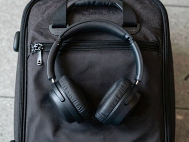 Flat-lay overhead of over-ear headphones resting on a carry-on bag handle, airport terminal floor visible at edges, consistent studio-grade natural light, minimal props