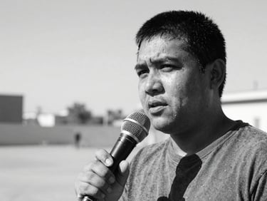 Close-up black and white portrait of a sound recordist holding a shotgun microphone outdoors, high contrast, documentary style.